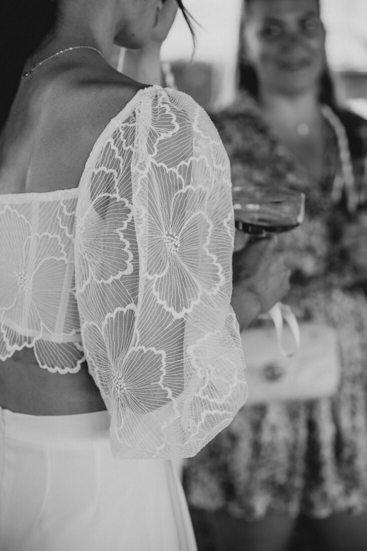 Nahaufnahme der floralen Spitze am Ärmel eines modernen Braut-Zweiteilers in Schwarz-Weiß bei einer Hochzeit am Bodensee.