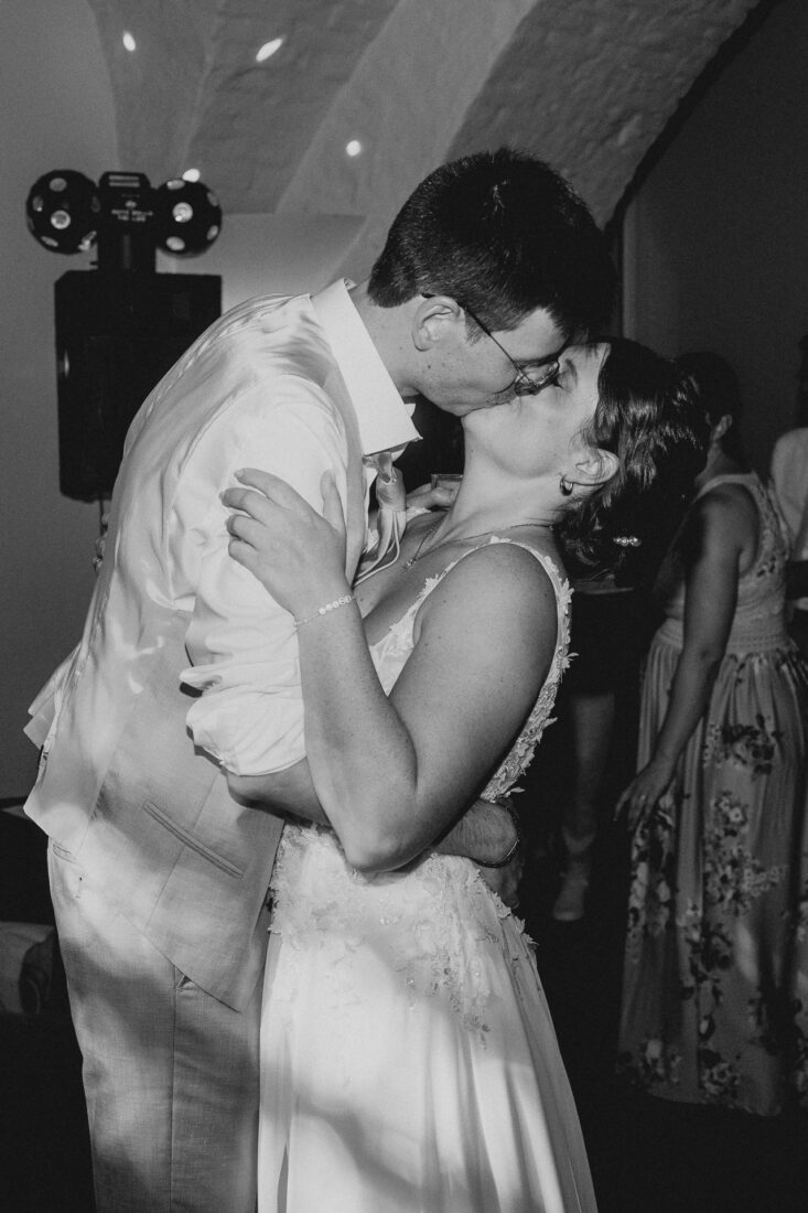 Schwarz-Weiß-Aufnahme des Brautpaares beim innigen Kuss während der Hochzeitsfeier am Abend.