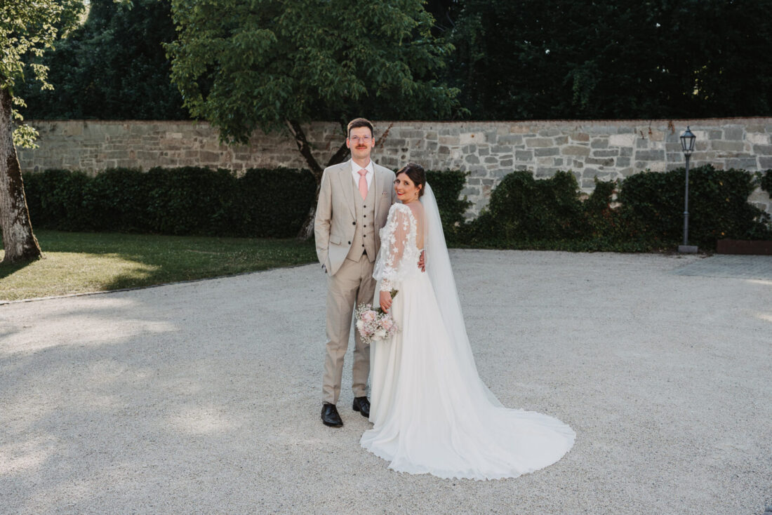 Das Brautpaar posiert vor einer historischen Steinmauer im Garten von Schloss Marbach bei Wangen.