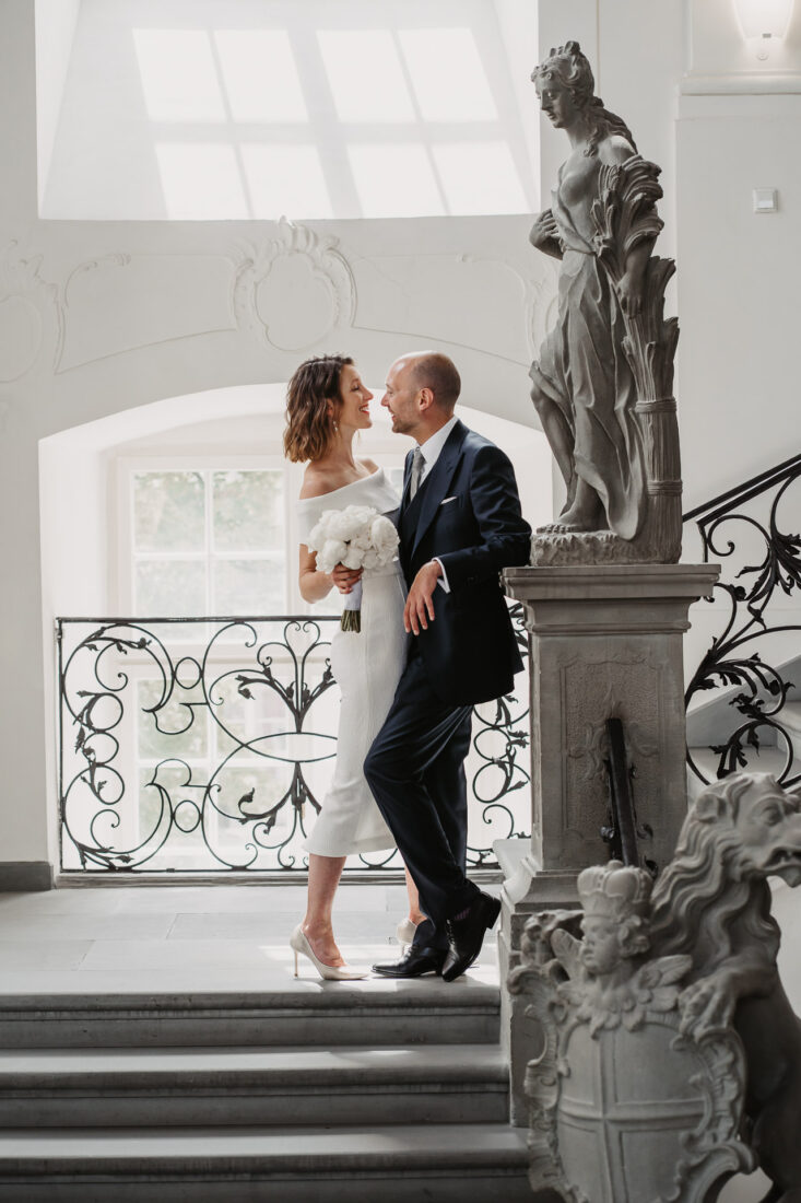 Inniges Porträt des Brautpaares zwischen Barock-Skulpturen im hellen Schlossflur in Meersburg am Bodensee.