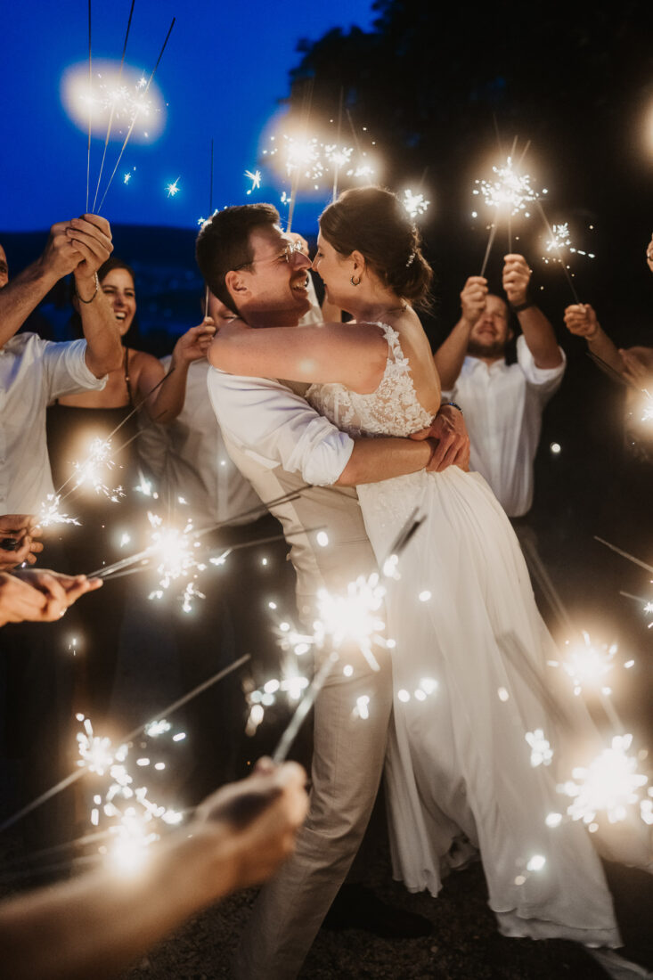 Der Bräutigam hebt die Braut hoch, umgeben von jubelnden Gästen und Wunderkerzen bei der Feier in Wangen auf Schloss Marbach.