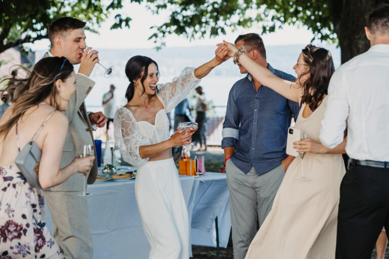 Das Brautpaar lacht und tanzt mit Freunden während des Empfangs am Museumssaal Überlingen, im Hintergrund ist der Bodensee erkennbar.