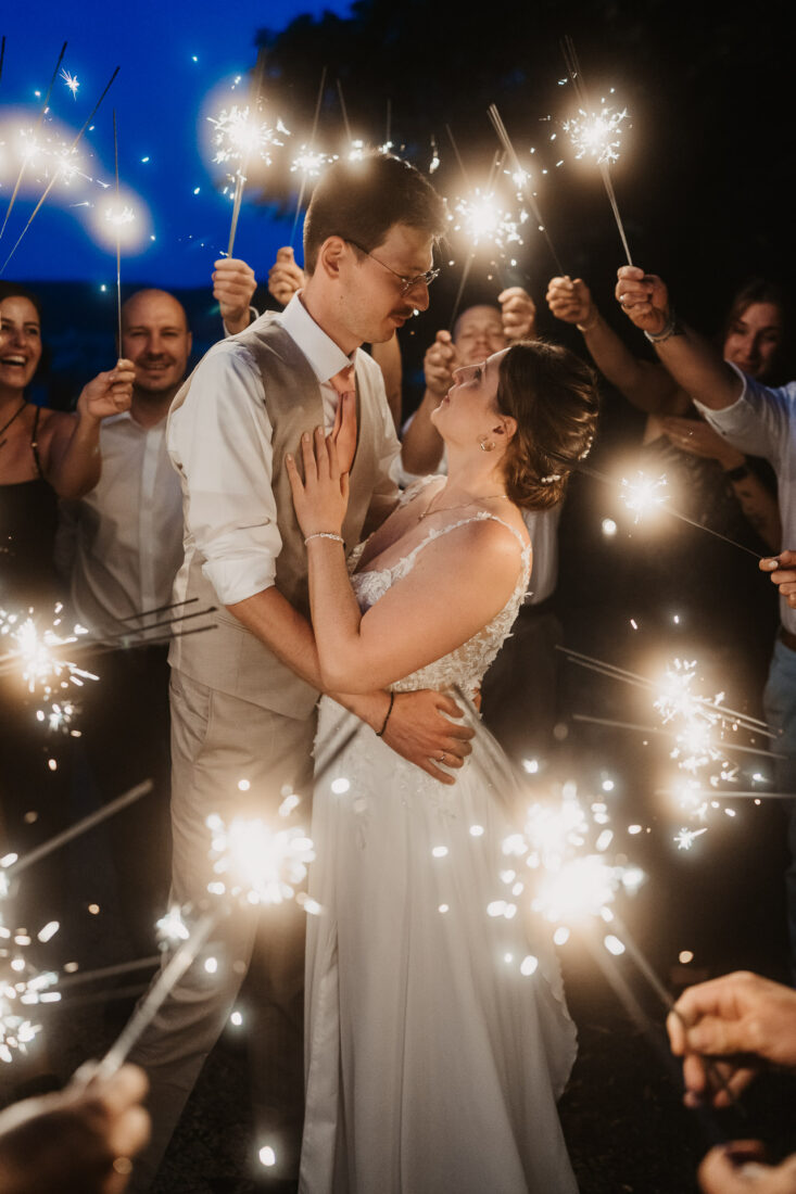 Braut und Bräutigam stehen in einem Spalier aus brennenden Wunderkerzen während ihrer Hochzeitsfeier am Bodensee.