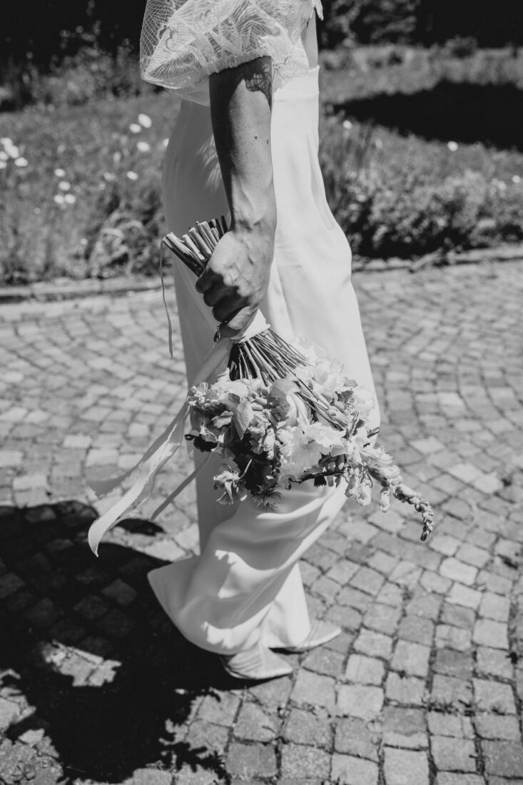 Schwarz-Weiß Detailfoto des Brautstraußes in den Händen der gehenden Braut.