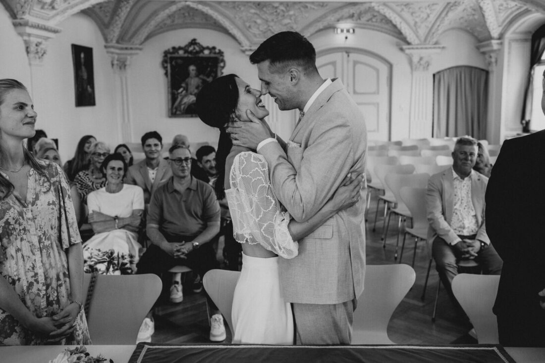 Emotionales Brautpaar lacht während der standesamtlichen Trauung im Museumssaal.