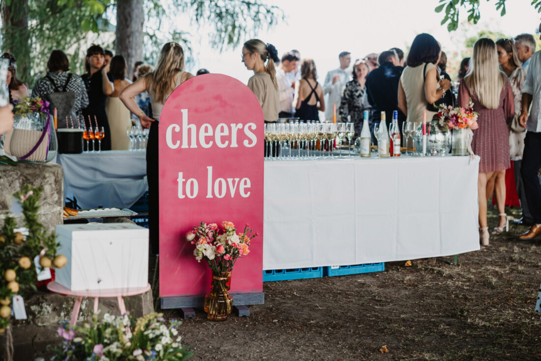 Pinkes Willkommensschild mit der Aufschrift „cheers to love“ beim Sektempfang im Garten des Museumssaals in Überlingen.
