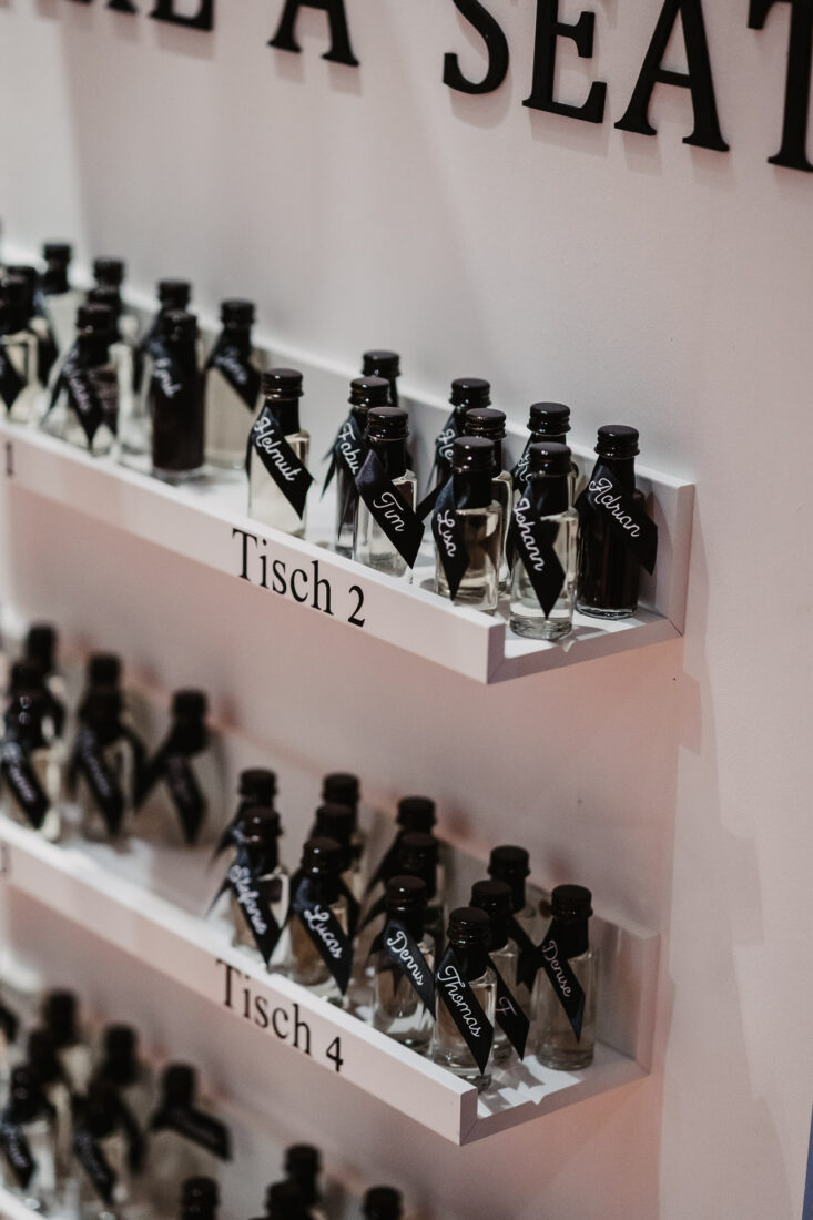 Detail des Sitzplans mit kleinen Schnapsflaschen, auf denen die Namen graviert sind.