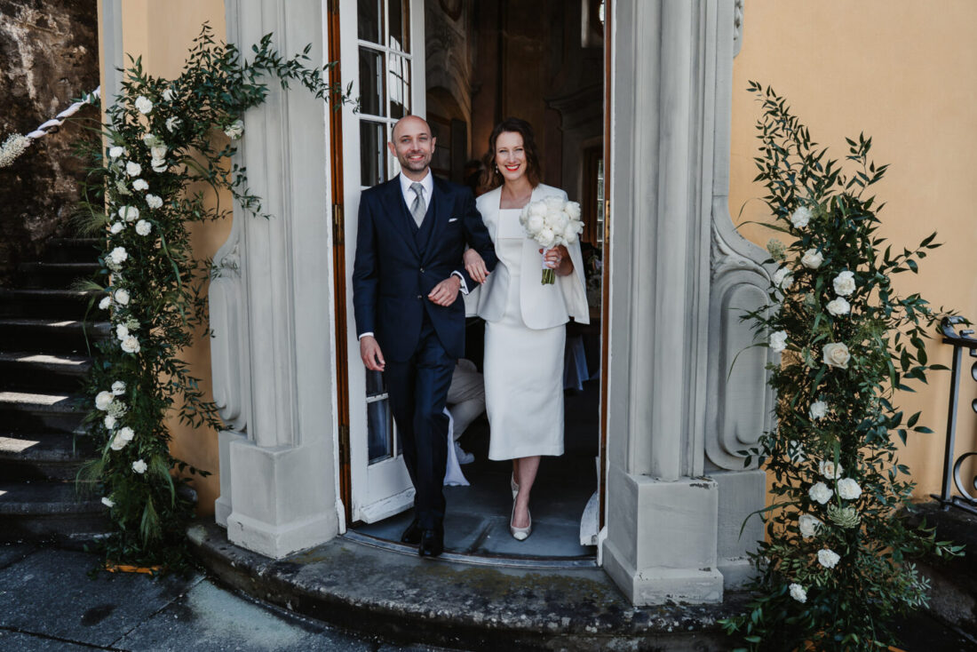 Strahlendes Brautpaar schreitet nach der Trauung durch die Türe des Teehauses des Schlosses Meersburg nach draußen.