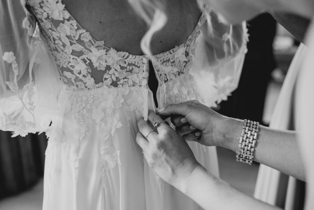 Detailaufnahme in Schwarz-Weiß: Die Braut wird im Schloss Marbach in ihr Spitzenkleid geknöpft.