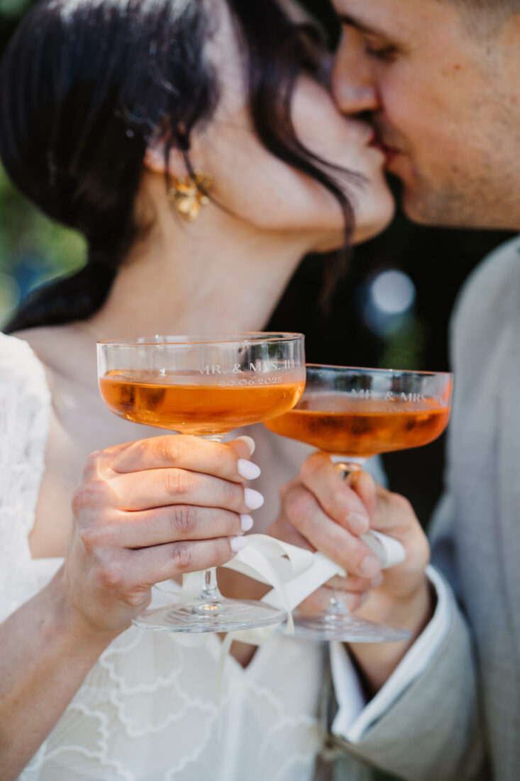 Detailaufnahme von zwei Sektgläsern mit Gravur "Mr. & Mrs." vor dem küssenden Brautpaar.