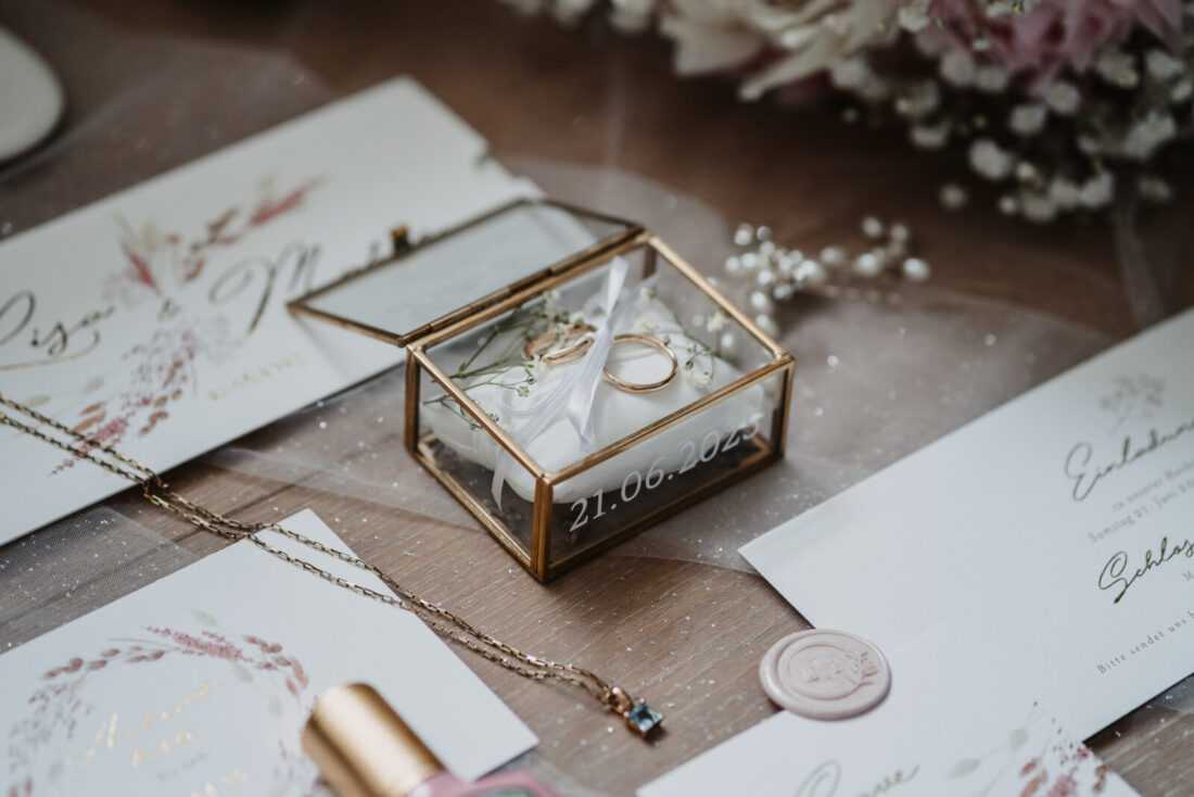 Goldene Eheringe in einer Glasbox mit dem Datum neben der Hochzeitspapeterie im Schloss Marbach.