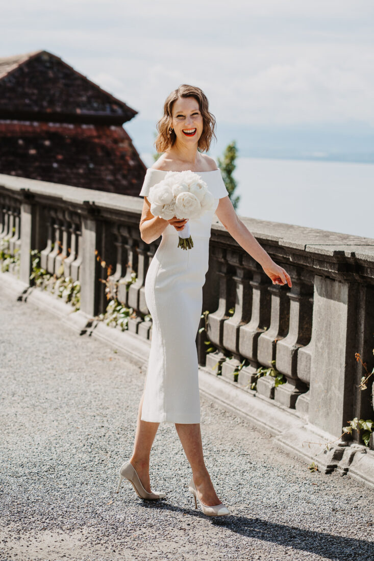 Detailaufnahme einer strahlenden Braut mit einem Pfingstrosen-Brautstrauß auf der Schlossterrasse mit Blick auf den Bodensee.