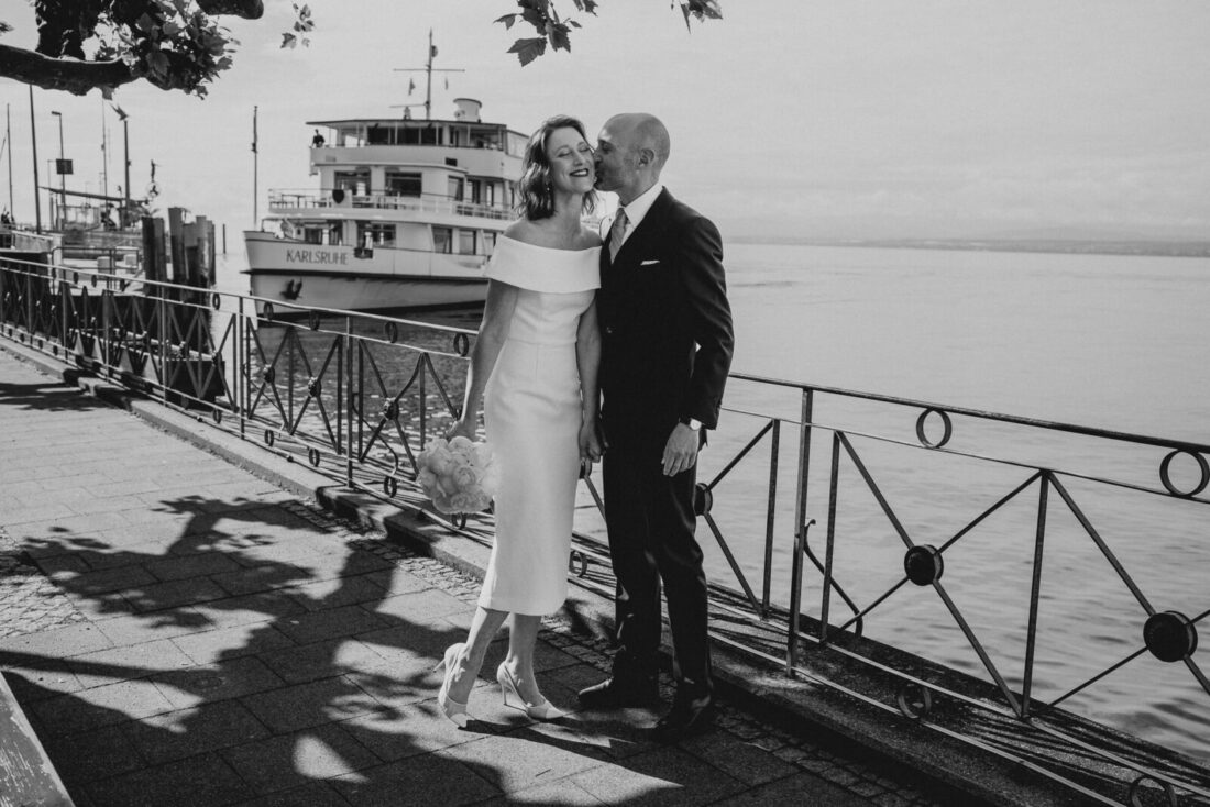 Brautpaar küsst sich am Ufer in Meersburg, im Hintergrund legt das Bodensee-Schiff MS Karlsruhe an.