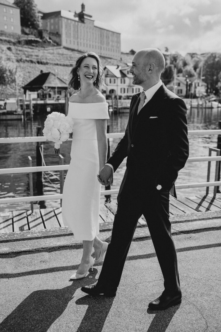 Hochzeitsfotografie in Meersburg: Paar läuft Hand in Hand am Schiffsanleger entlang, im Hintergrund die historische Kulisse der Altstadt.