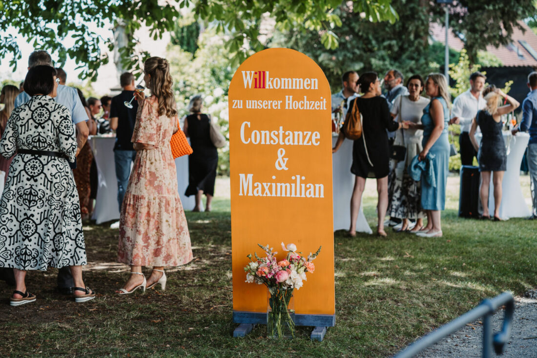 Orangefarbenes Willkommensschild "Constanze & Maximilian" beim Sektempfang am Museumssaal in Überlingen.