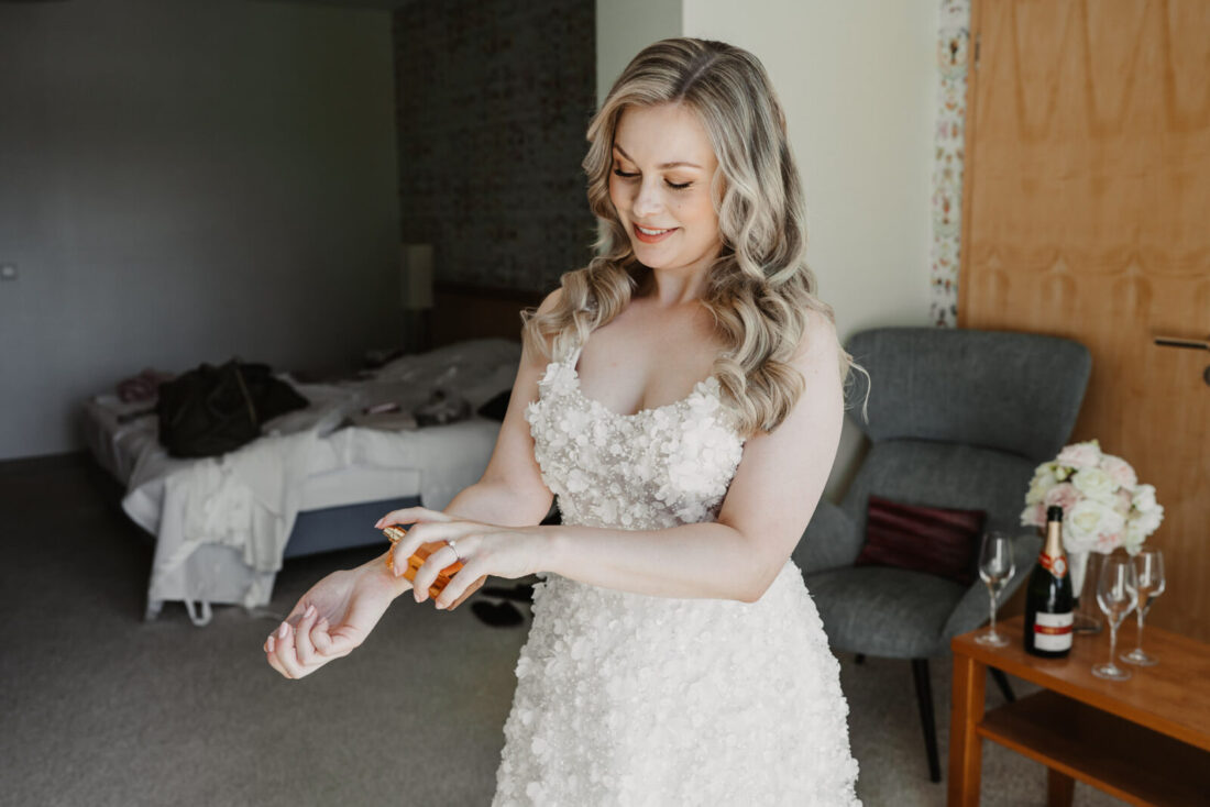 Die Braut trägt ihr Parfum auf die Arminnenflächen auf und lächelt freudig dabei.