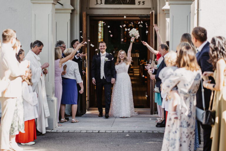 Brautpaar verlässt freudig die Kirche in Bodman-Ludwigshafen während Gäste Blumen werfen