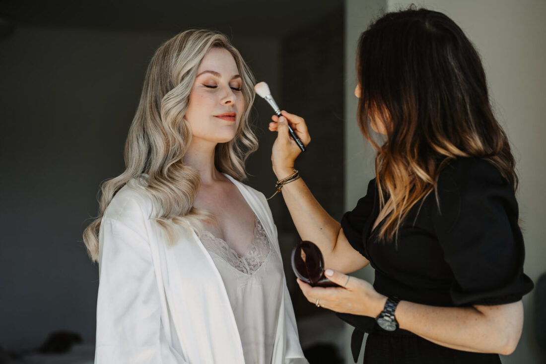 Die Braut bekommt von ihrer Stylistin das Make-Up aufgetragen.