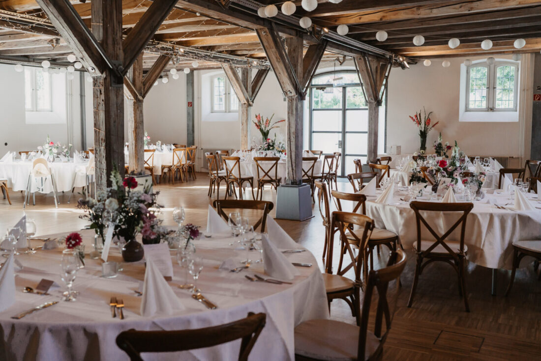 Festlich dekorierter Hochzeitssaal im Zollhaus Ludwigshafen mit runden Tischen und Holzträgern